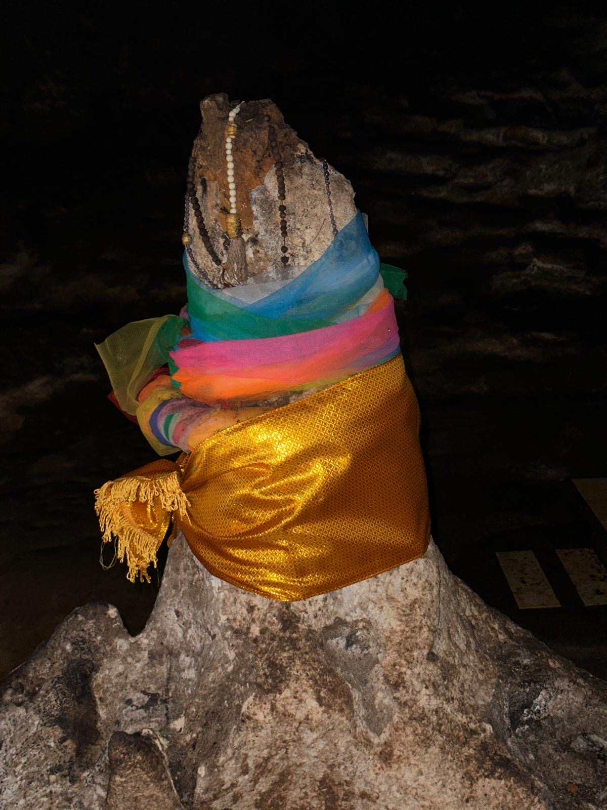 Eine Felsformation in einer Höhle in Kambodscha ist mit bunten Tüchern und Ketten geschmückt.