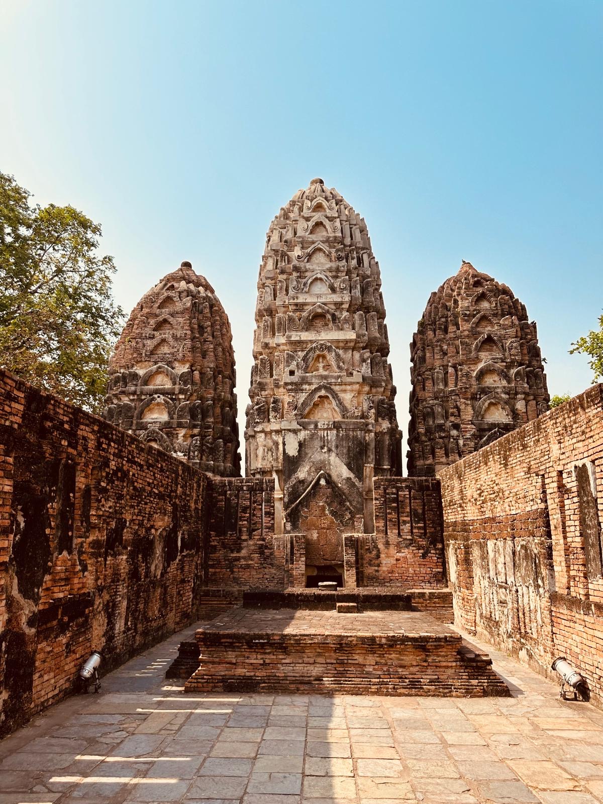 Drei verzierte Tempeltürme des Wat Si Sawai in Sukhothai, eingerahmt von alten Ziegelmauern.